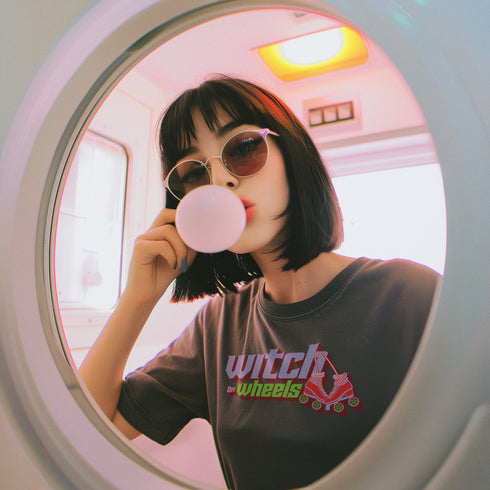 Gray t-shirt with "Witch on Wheels" text in purple and green, featuring a red roller skate graphic. The vintage-style design has a slightly faded look on a relaxed-fit unisex tee.